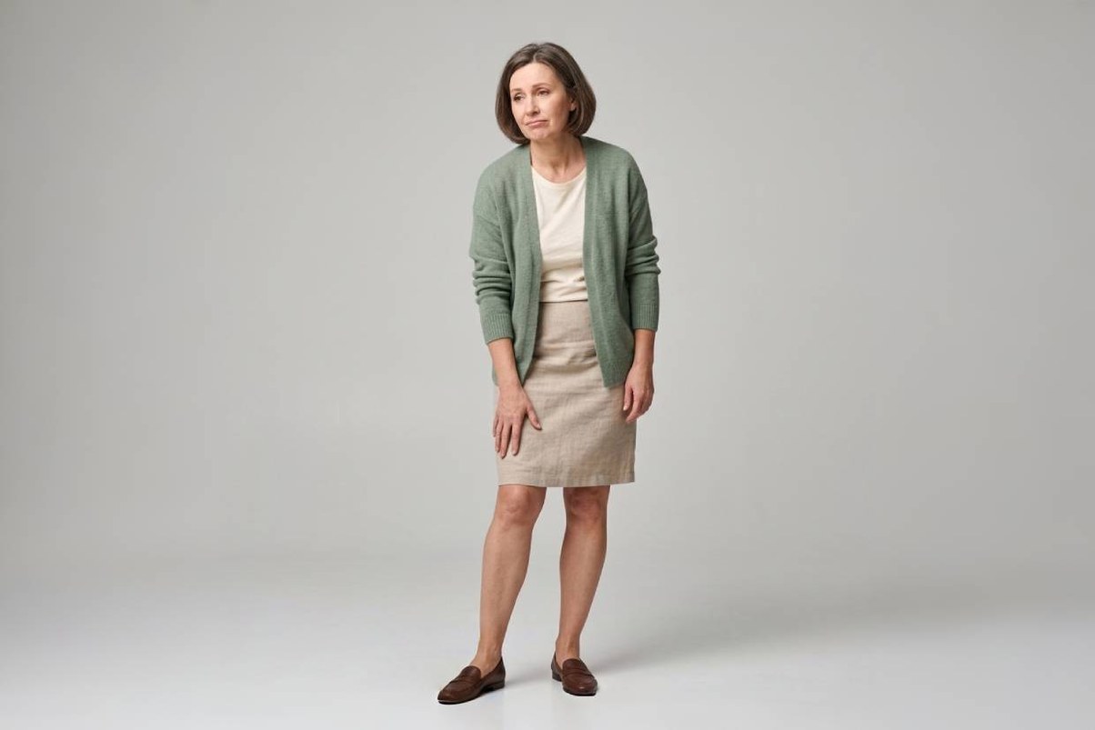 Femme en cardigan vert tenant sa cuisse, studio neutre — jambes lourdes et insuffisance veineuse, Pharmacie Charnal Quéven