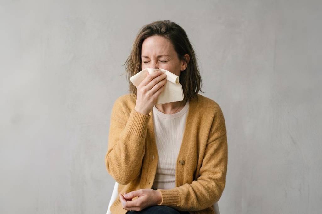 Femme en cardigan moutarde se mouchant, symptome typique de l'allergie au pollen en Bretagne