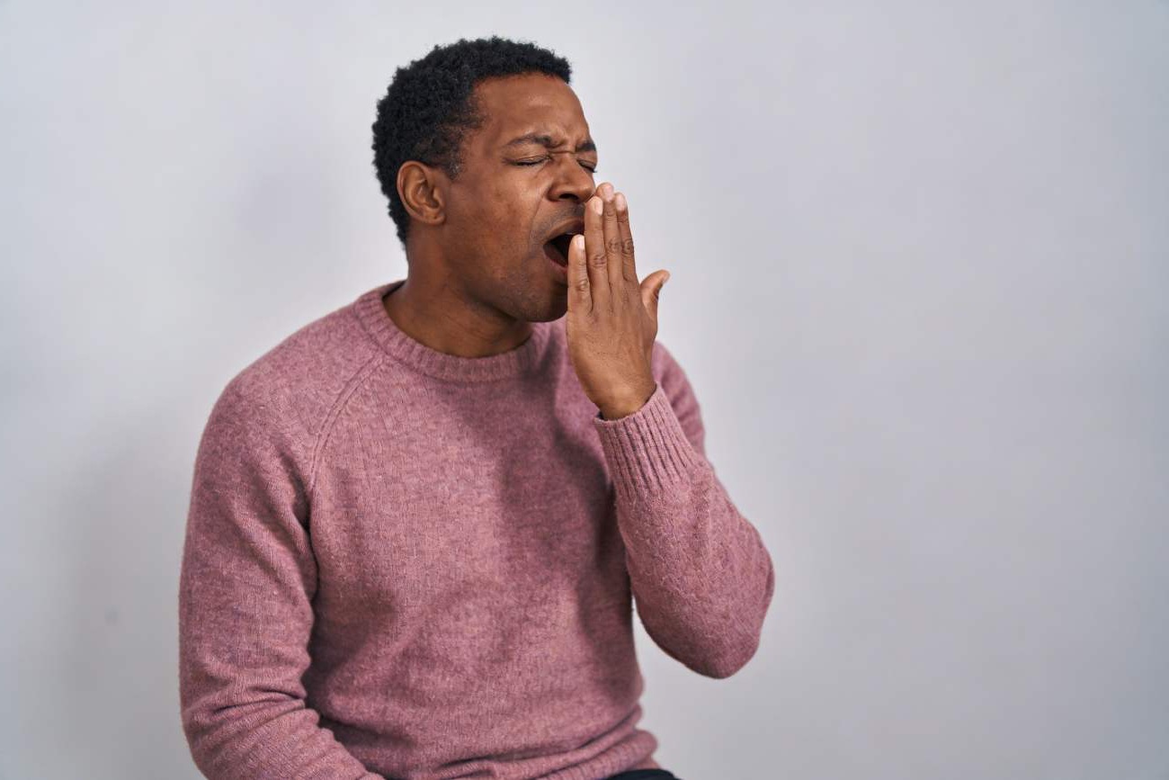 Homme bâillant en pull mauve, illustrant les troubles du sommeil et le manque de repos