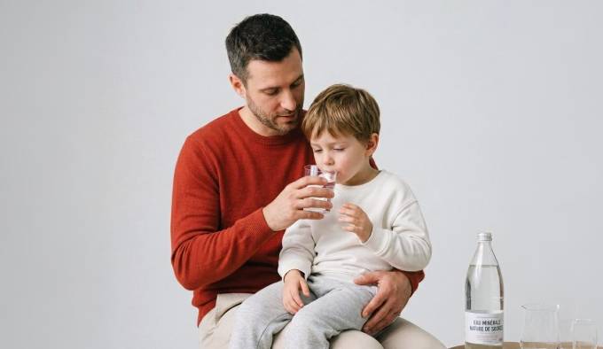 Père aidant son enfant à boire de l'eau pour se réhydrater pendant une gastro-entérite
